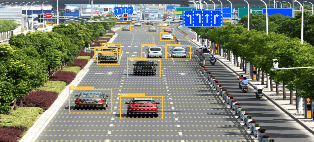 An urban road scene with multiple vehicles and motorbikes detected and highlighted by yellow bounding boxes labeled 'CAR,' showing automated data annotation in progress. The road is flanked by green trees and shrubs, with blue traffic signs visible in the background.